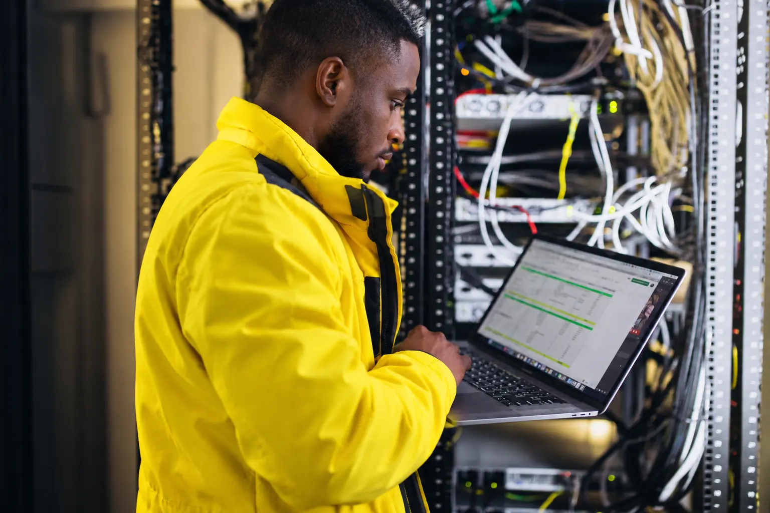 IT technician checking a laptop beside network equipment